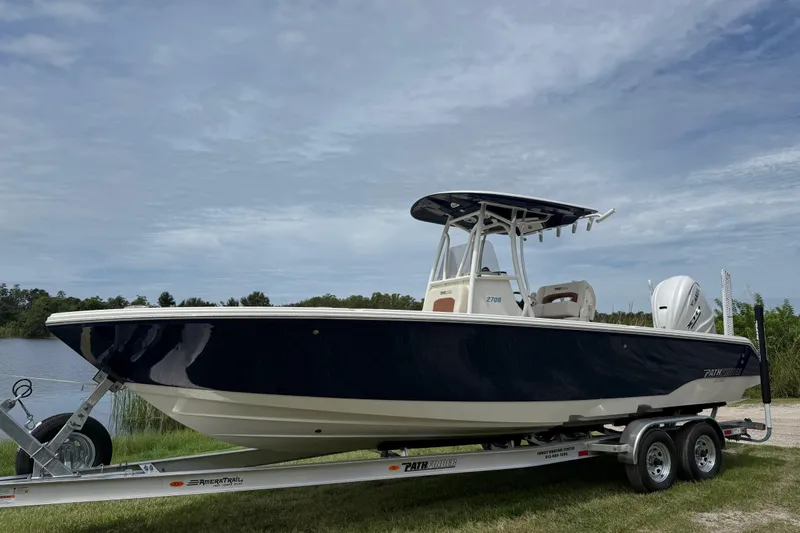 The Image of 2026 Pathfinder 2700 Open boat on trailer by a lake, under cloudy sky. - 0