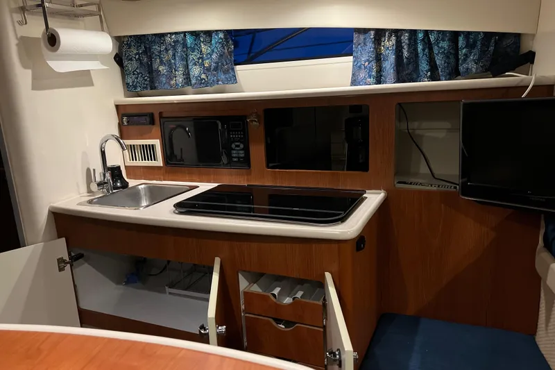 Slide: The Image of 2003 Bayliner 285 boat interior kitchen with sink, stove, microwave, and TV. - 16