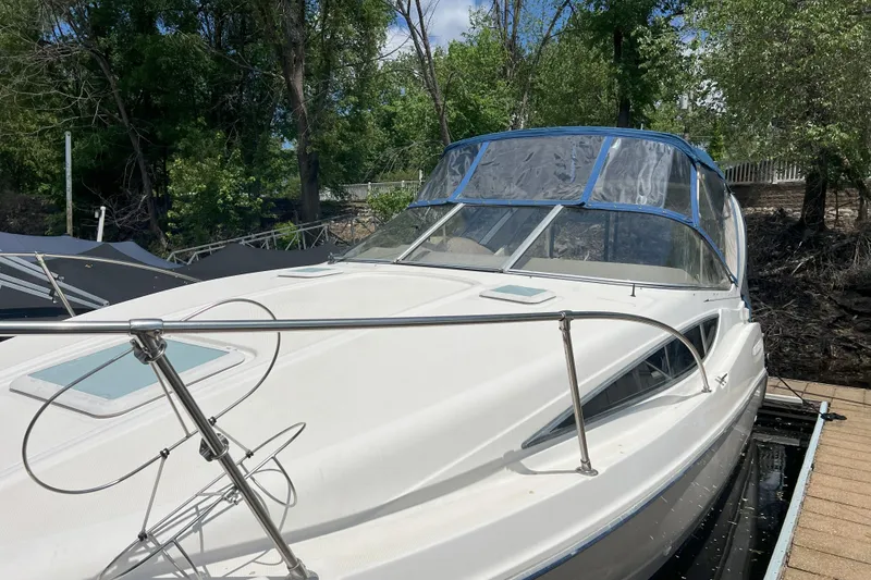 Slide: The Image of 2003 Bayliner 285 boat docked, featuring sleek design and clear canopy, surrounded by trees. - 9