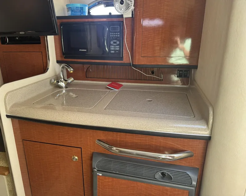 Slide: The Image of 2004 Sea Ray 280 Sundancer kitchenette with sink, microwave, and wooden cabinetry. - 17