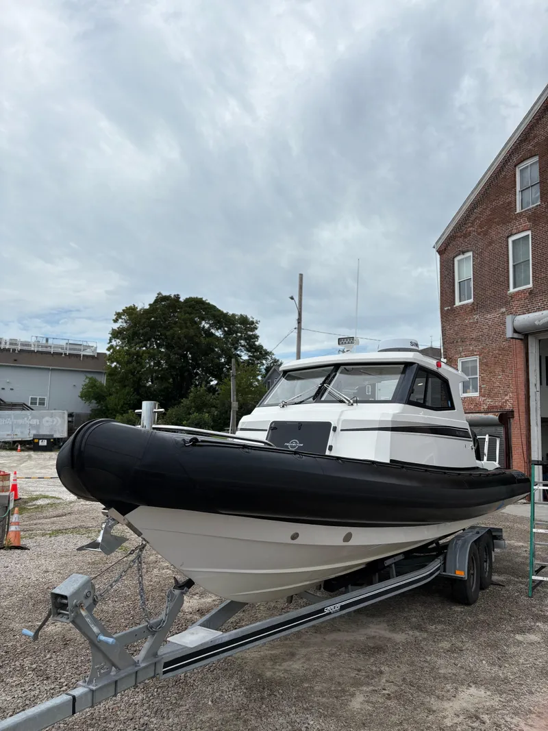 Slide: The Image of 2020 Protector 310 Targa boat on trailer, parked near a brick building. - 7