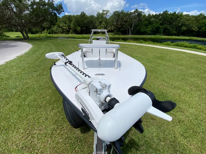 Slide: The Image of 2020 East Cape 18 EVO boat on grass with trolling motor, surrounded by trees and blue sky. - 21