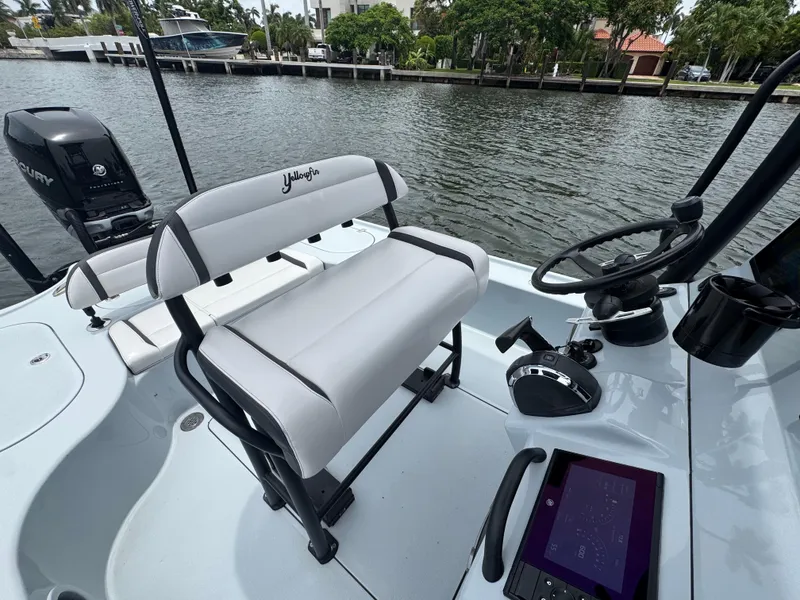 Slide: The Image of 2019 Yellowfin 24 Bay CE boat interior with steering wheel and seating, docked by a canal. - 14
