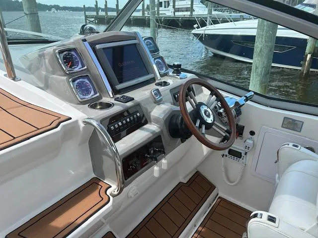 Slide: The Image of 2014 Chaparral 310 Signature boat cockpit with modern controls and wood accents, docked by the water. - 11