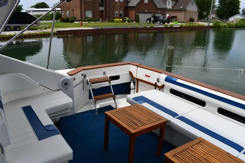 Slide: The Image of 1989 Sea Ray 390 Express Cruiser with spacious deck, wooden tables, and comfortable seating by the water. - 23