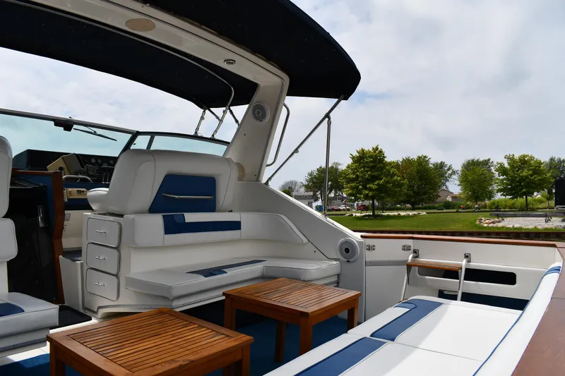 Slide: The Image of 1989 Sea Ray 390 Express Cruiser interior with seating and wooden tables, docked near greenery. - 26