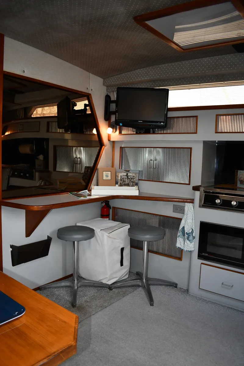 Slide: The Image of 1989 Sea Ray 390 Express Cruiser interior with kitchenette, stools, and mounted TV. - 44