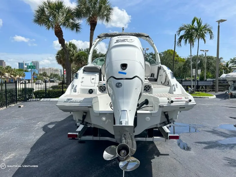 Slide: The Image of 2024 Crownline E290 XS boat, rear view, parked on a sunny day with palm trees. - 2