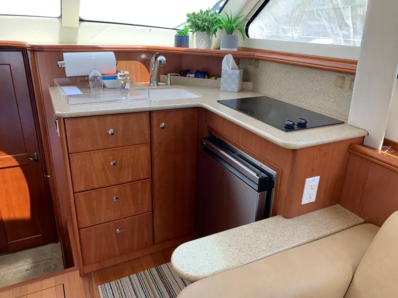 Slide: The Image of 2012 Silverton 33 Sport Coupe yacht kitchen with wood cabinetry, sink, stove, and mini fridge. - 15