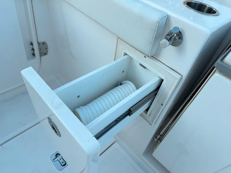 Slide: The Image of 2022 Pursuit DC 365 Dual Console boat with open storage drawer and coiled hose. - 15