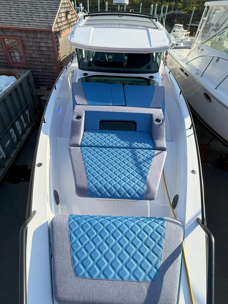 Slide: The Image of 2024 Axopar Cross Cabin boat with blue cushioned deck, docked beside other vessels. - 4