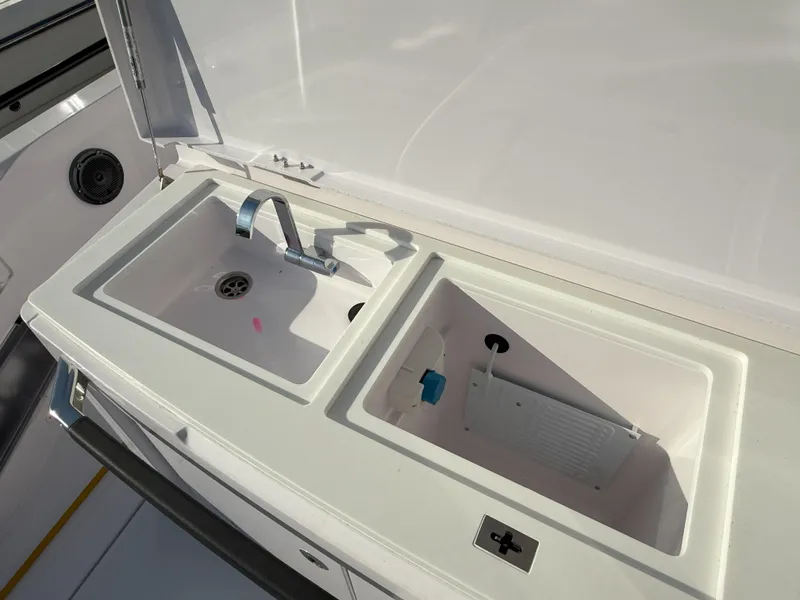 Slide: The Image of 2024 Axopar Cross Cabin boat with open storage compartment, docked at a marina. - 14