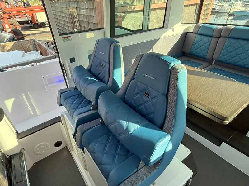 Slide: The Image of 2024 Axopar Cross Cabin interior with blue seating and dining area, featuring large windows. - 35