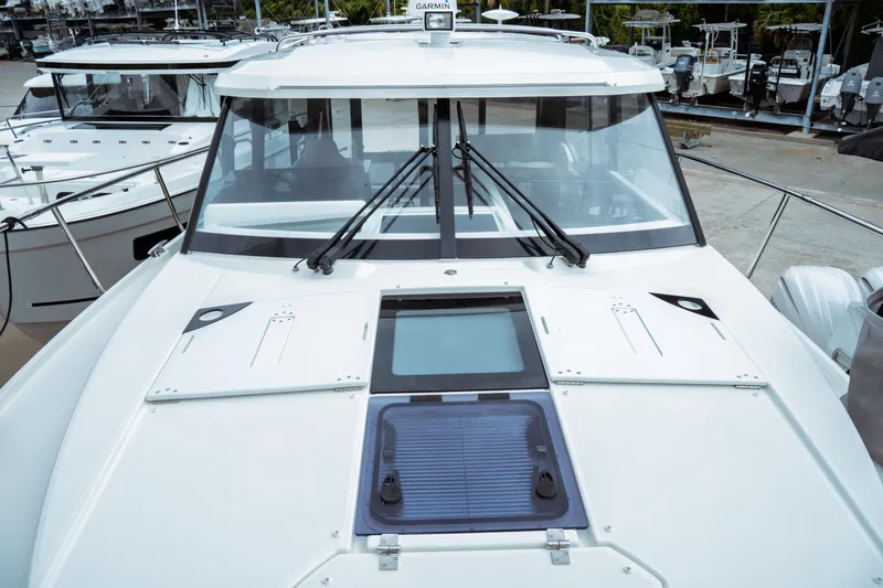 Slide: The Image of 2023 Jeanneau NC 1095 boat deck with windshield and hatches in marina setting. - 14