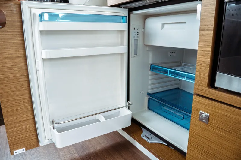 Slide: The Image of Open refrigerator inside 2023 Jeanneau NC 1095 boat, featuring wooden cabinetry and modern design. - 51