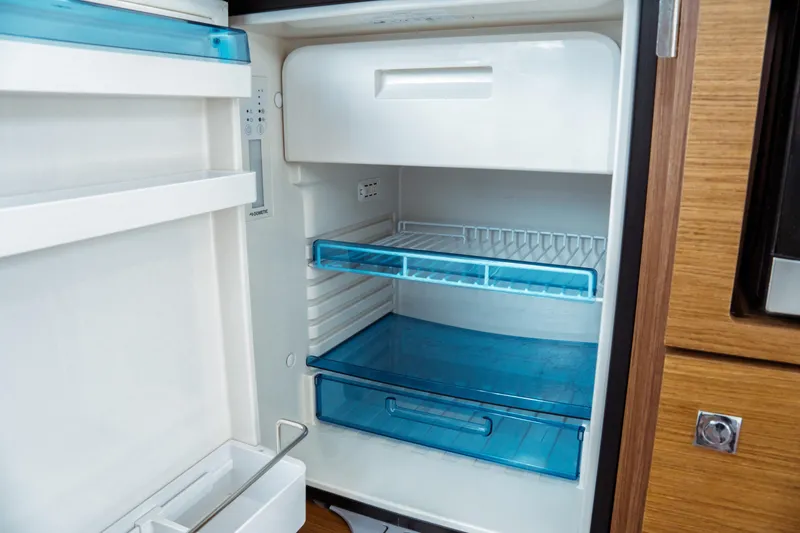 Slide: The Image of Open fridge inside 2023 Jeanneau NC 1095 boat, featuring blue shelves and modern design. - 52