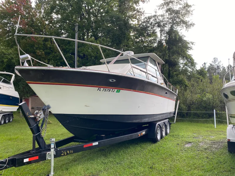 Slide: The Image of 1976 Slickcraft 28 Cruiser boat on trailer, parked on grass with trees in background. - 1