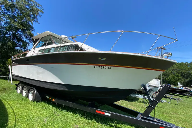 Slide: The Image of 1976 Slickcraft 28 Cruiser boat on trailer, parked on grass under clear blue sky. - 2
