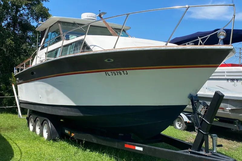 Slide: The Image of 1976 Slickcraft 28 Cruiser boat on trailer, parked on grass under clear blue sky. - 3