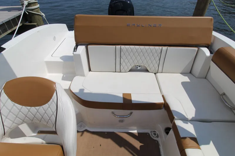 Slide: The Image of 2022 Bayliner DX2000 boat interior with tan and white seating, docked by the water. - 13