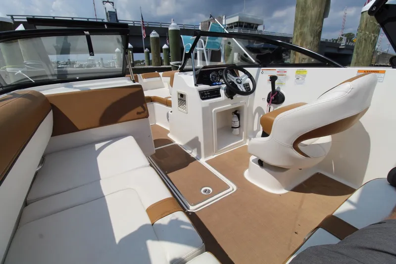 Slide: The Image of 2022 Bayliner DX2000 boat interior with tan and white seating, steering console, and docked background. - 19