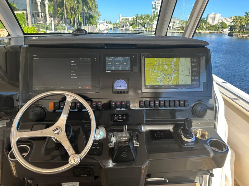 Slide: The Image of 2018 Pursuit 408S boat helm with navigation screens and steering wheel, overlooking a scenic waterway. - 13
