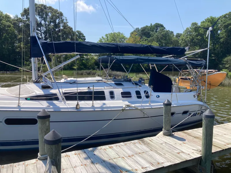 Slide: The Image of Sailboat docked at a marina, Hunter 410 model, 2002, with blue covers and lush greenery. - 26