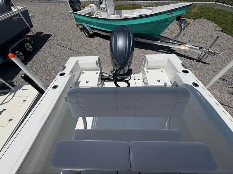 Slide: The Image of 2026 Parker 210 COASTAL boat with outboard motor, parked on gravel with another boat nearby. - 7