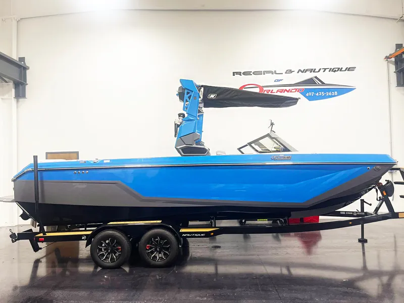 The Image of 2025 Nautique Super Air Nautique GS24 boat in showroom, blue exterior, on trailer. - 1