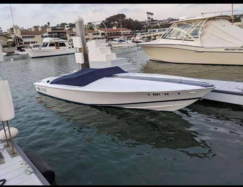 Slide: The Image of 2005 Donzi boat docked in marina, covered with blue tarp, calm water surroundings. - 1