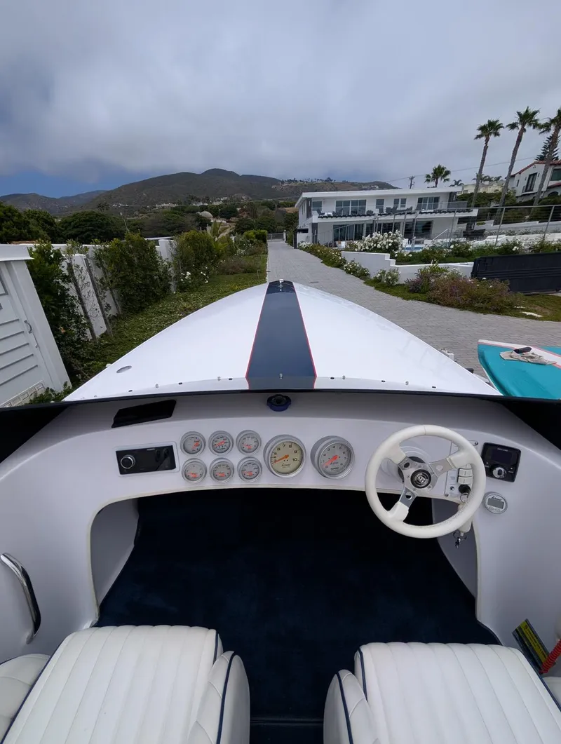 Slide: The Image of 2005 Donzi boat dashboard with gauges and steering wheel, parked near modern coastal homes. - 2