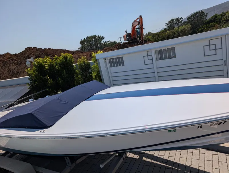 Slide: The Image of 2005 Donzi boat with blue cover, parked near construction site and greenery. - 3