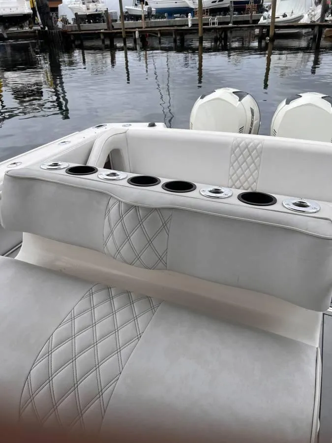 Slide: The Image of 1996 Intrepid 370 Cuddy boat interior with cushioned seating and cup holders at a marina. - 14