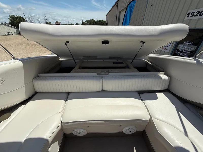 Slide: The Image of 2004 Crownline 266 BR boat interior with open storage compartment, white seating, and sunny weather. - 23