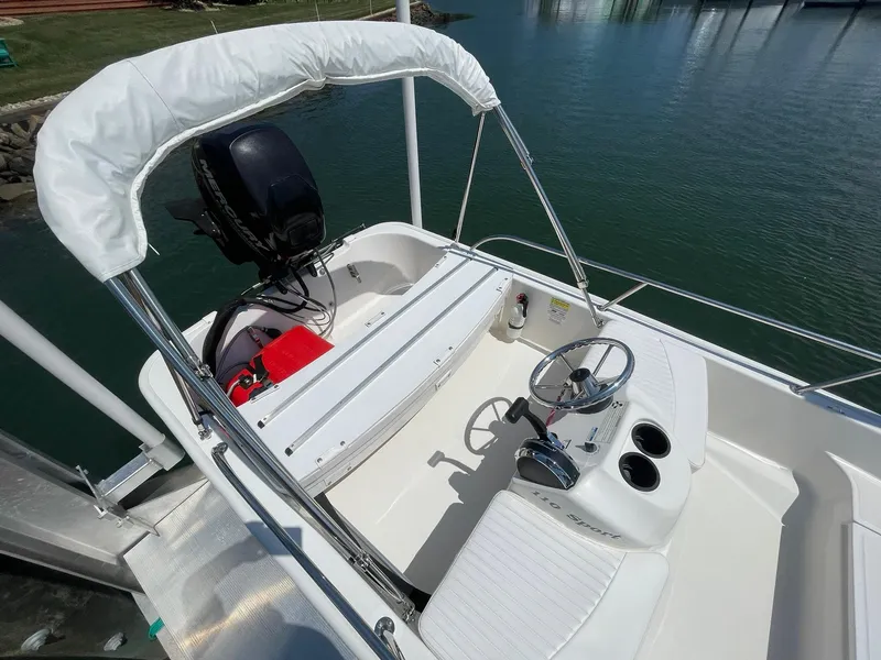 Slide: The Image of 2015 Boston Whaler 110 Sport boat interior with steering wheel and seating, docked on calm water. - 11