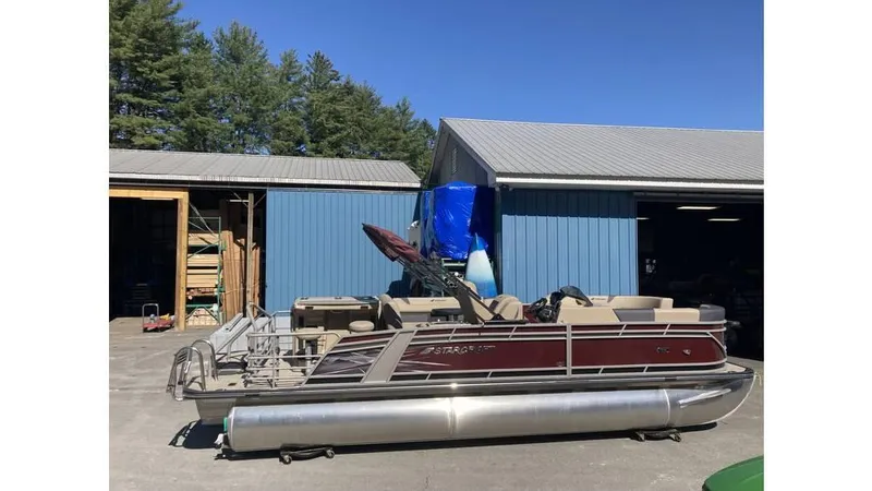 Slide: The Image of 2024 Starcraft CX 23 DL BAR pontoon boat parked outside a blue building. - 3