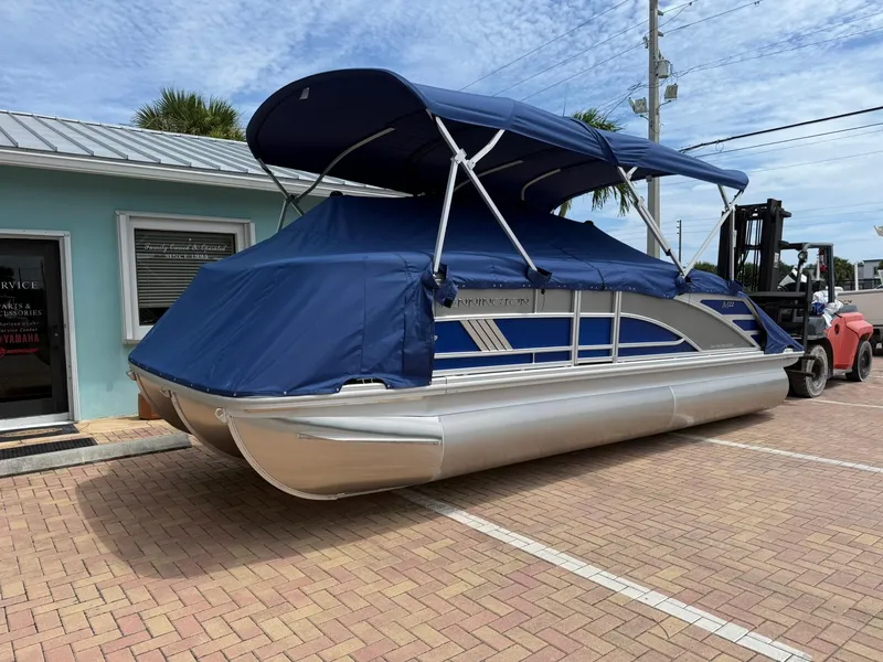 Slide: The Image of 2026 Bennington 22 MSB pontoon boat with blue cover parked outside a building. - 2