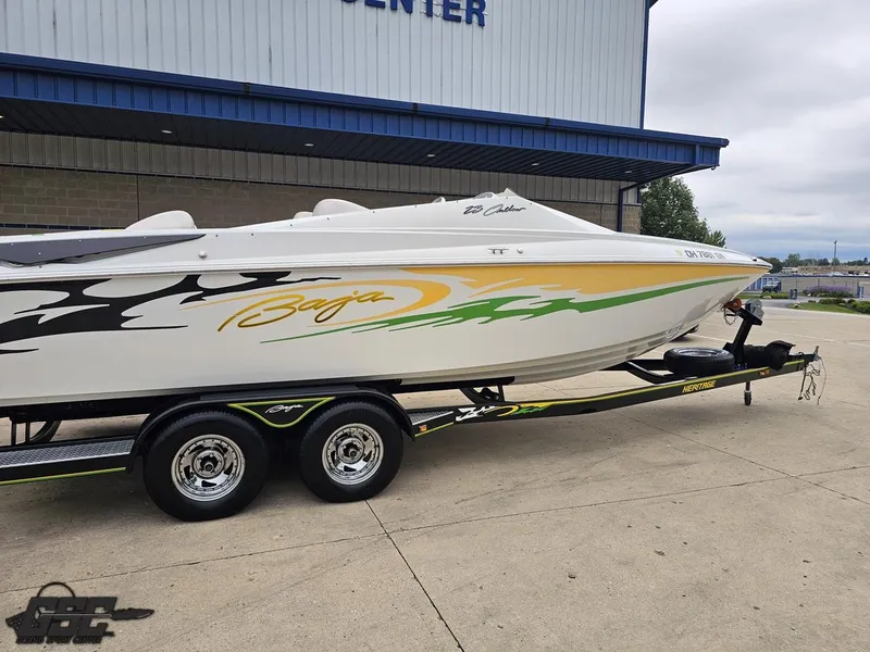 Slide: The Image of 2005 Baja 23 Outlaw speedboat on trailer, featuring vibrant graphics, parked outside a building. - 12