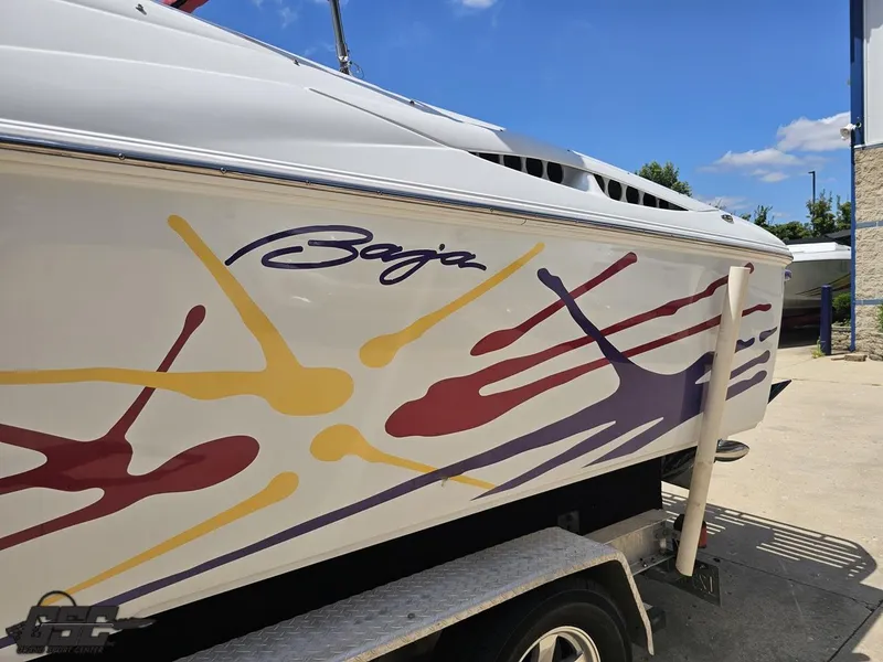 Slide: The Image of 2000 Baja 29 Outlaw boat with colorful graphics on a trailer under a clear blue sky. - 36