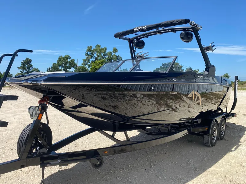 Slide: The Image of 2025 ATX Surf Boats 24 Type-S on trailer, sleek black design under clear blue sky. - 2