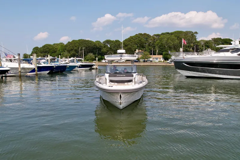 Slide: The Image of 2025 Nimbus T9 boat docked in a marina, surrounded by other boats and calm water. - 7