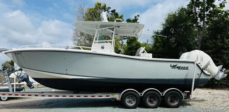 Slide: The Image of 2018 Mako 284 CC boat on trailer, parked outdoors, surrounded by trees. - 4
