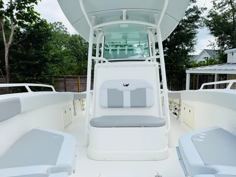 Slide: The Image of 2018 Mako 284 CC boat interior with cushioned seating and canopy, surrounded by greenery. - 6