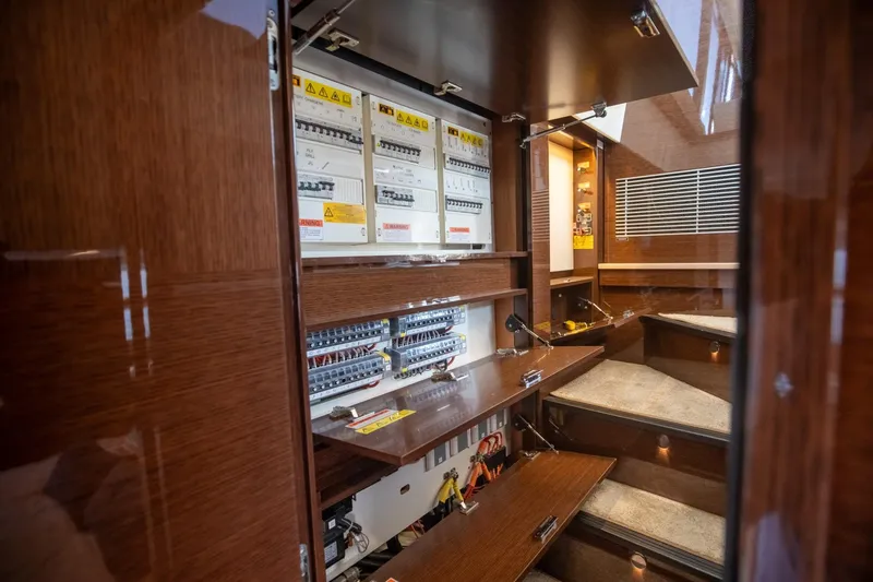 Slide: The Image of Electrical panel inside 2020 Prestige 590 Flybridge Cruiser, featuring wooden cabinetry and circuit breakers. - 48