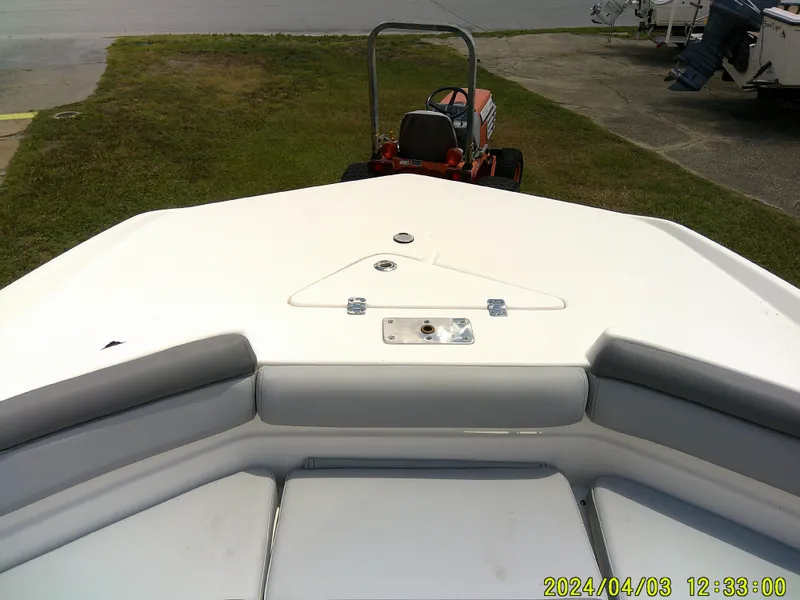 Slide: The Image of 2023 NauticStar 231 Hybrid boat bow with seating, parked near a lawn and tractor. - 20