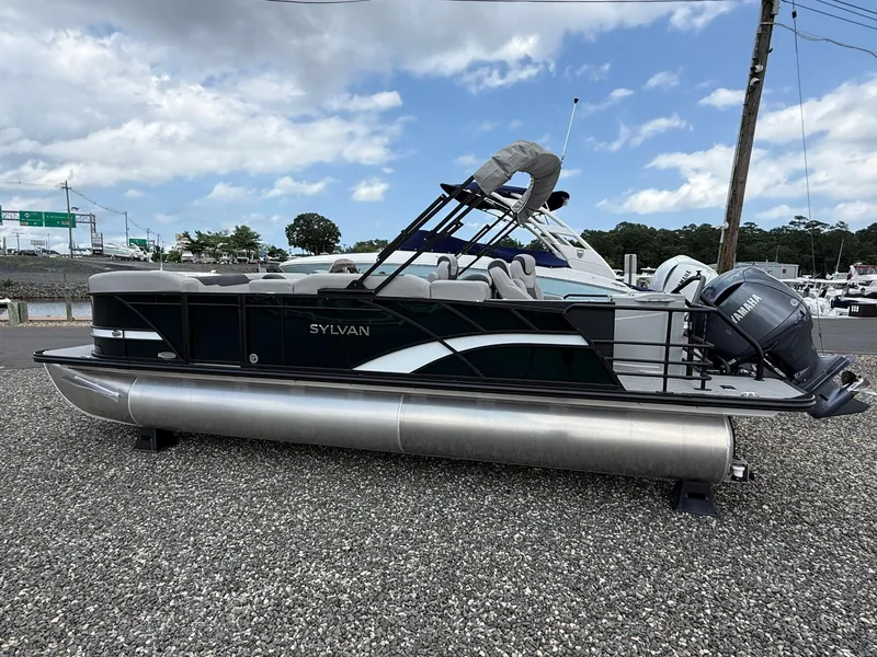 Slide: The Image of 2025 Sylvan L3 Party Fish pontoon boat on gravel lot, under cloudy sky. - 6