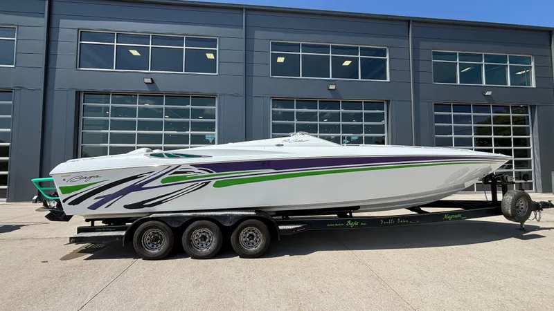 The Image of 2005 Baja 33 Outlaw speedboat with vibrant graphics on a trailer, parked outside a modern building. - 1