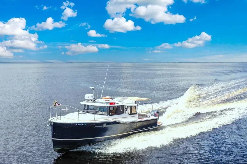 Slide: The Image of 2024 Ranger Tugs R-27 cruising on open water under a bright blue sky. - 0