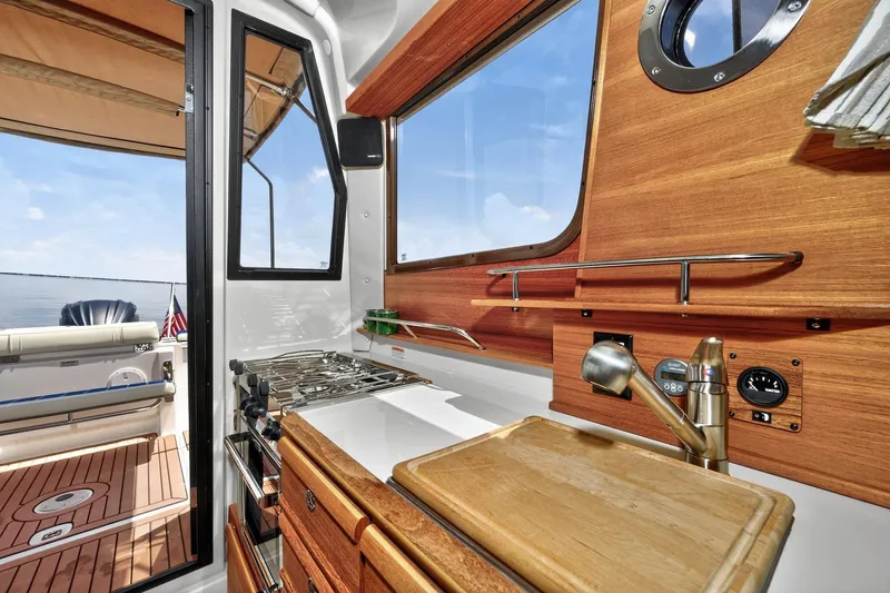 Slide: The Image of 2024 Ranger Tugs R-27 interior kitchen with wooden cabinetry and ocean view. - 28