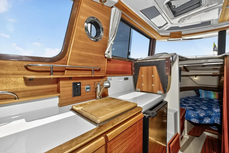 Slide: The Image of 2024 Ranger Tugs R-27 interior with wooden cabinetry, compact kitchen, and cozy sleeping area. - 29